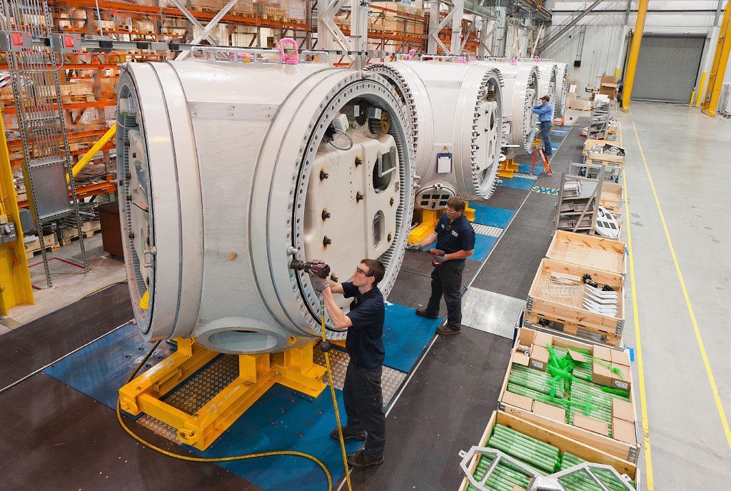 Man in blue jacket standing beside gray and blue industrial machine. Americans wind turbines manufacturing - Nordex USA manufacturing facility - Jonesboro, Arkansas.