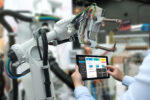 Engineer hand using tablet, heavy automation robot arm machine in smart factory industrial with tablet real time monitoring system application. Machine learning operations (MLOps)