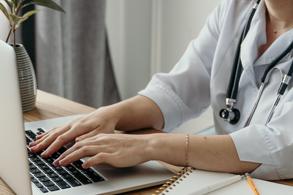 A Woman Doctor Typing Health Informatics on Her Laptop