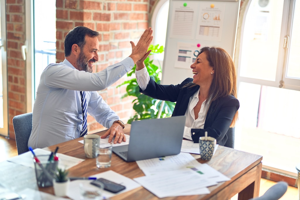 Two middle age business workers smiling happy and confident. Businessman and Businesswoman working together with smile on face hand giving high five at the office.