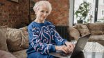 Photo of an elderly woman in a blue top typing on a laptop