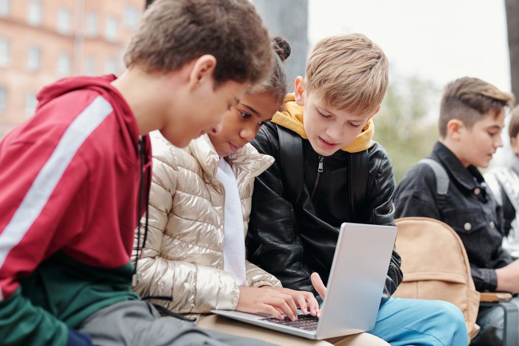 Group of children studying together on a laptop outdoors, fostering collaboration.