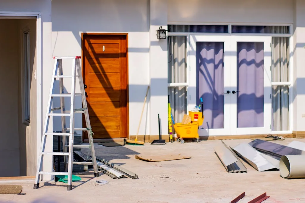 Front entrance of a house undergoing renovation with a ladder, cleaning supplies, construction materials, and tools arranged around the exterior. The image represents a residential home improvement project focused on sustainable remodeling, energy-efficient upgrades, smart home modernization, and eco-friendly property improvements designed to enhance comfort, efficiency, and long-term cost savings.