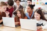 School students actively collaborate on laptops in an educational environment with guidance from a teacher.