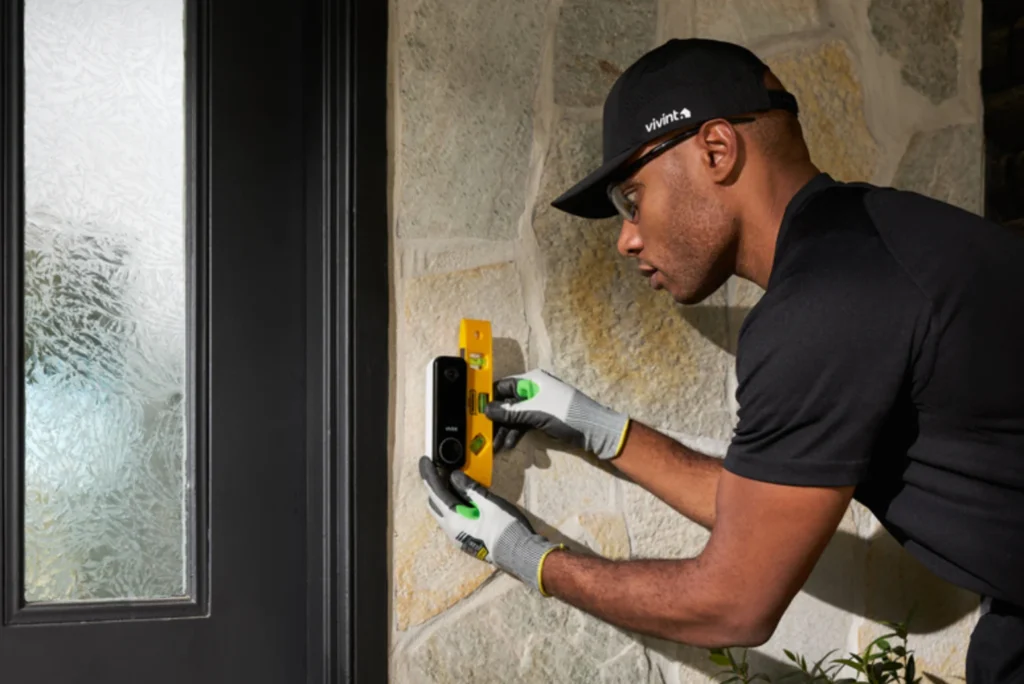 Vivint technician installing and leveling a smart doorbell beside a front door, illustrating smart home security installation and connected home automation.